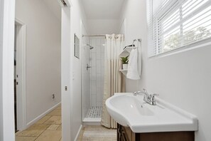 A narrow bathroom with a shower, a sink, and a small window with blinds. - Historic Hideaway - Downtown/Night of Lights getaway! (St. Augustine)