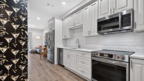 A modern kitchen with white cabinets, a stainless steel refrigerator, a microwave, and an oven. - Cozy Condo with Rooftop Views (Bay St. Louis)