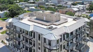 A multi-story building with balconies, a flat roof, and a view of a bridge and water in the background. - Cozy Condo with Rooftop Views (Bay St. Louis)