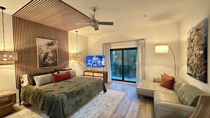 A modern bedroom with a bed, a sofa, a TV, and a balcony with a view. - Cozy Condo with Rooftop Views (Bay St. Louis)