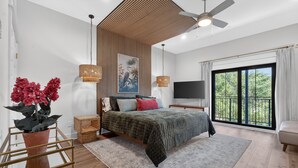 A modern bedroom with a bed, a TV, a large window, and a ceiling fan. - Cozy Condo with Rooftop Views (Bay St. Louis)