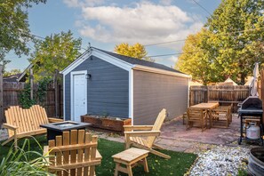 A backyard with a shed, wooden chairs, a table, and a grill. - Cozy central cottage! Fire pit, Theater Room & 420 Friendly! (Denver)