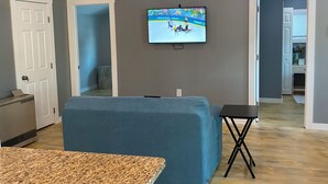 Un salon spacieux avec un plafond en bois, un téléviseur fixé au mur et un canapé bleu.