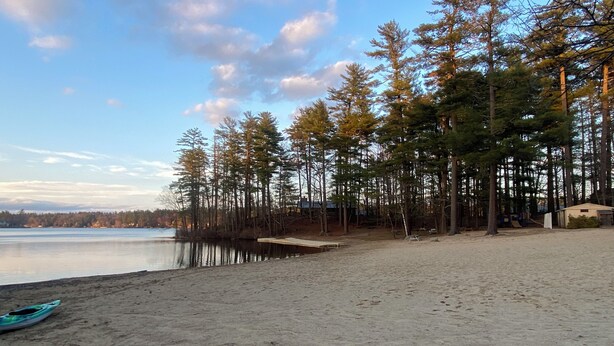 Une plage de sable fin, un kayak, des arbres denses et un lac paisible.