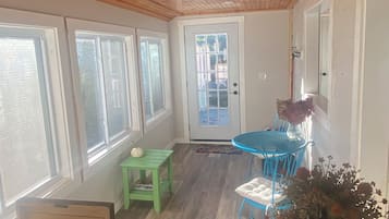 Una habitación con techo de madera, una mesa de comedor con sillas, una mesita verde y una puerta con paneles de vidrio.