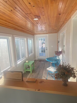 Una habitación con techo de madera, una mesa de comedor con sillas, una mesita verde y una puerta con paneles de vidrio.