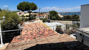 Terraço no telhado com piso de azulejos, guarda-corpo de metal e vista para uma cidade costeira.
