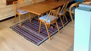 Uma sala de jantar com mesa e cadeiras de madeira, um tapete estampado e luminárias pendentes amarelas.