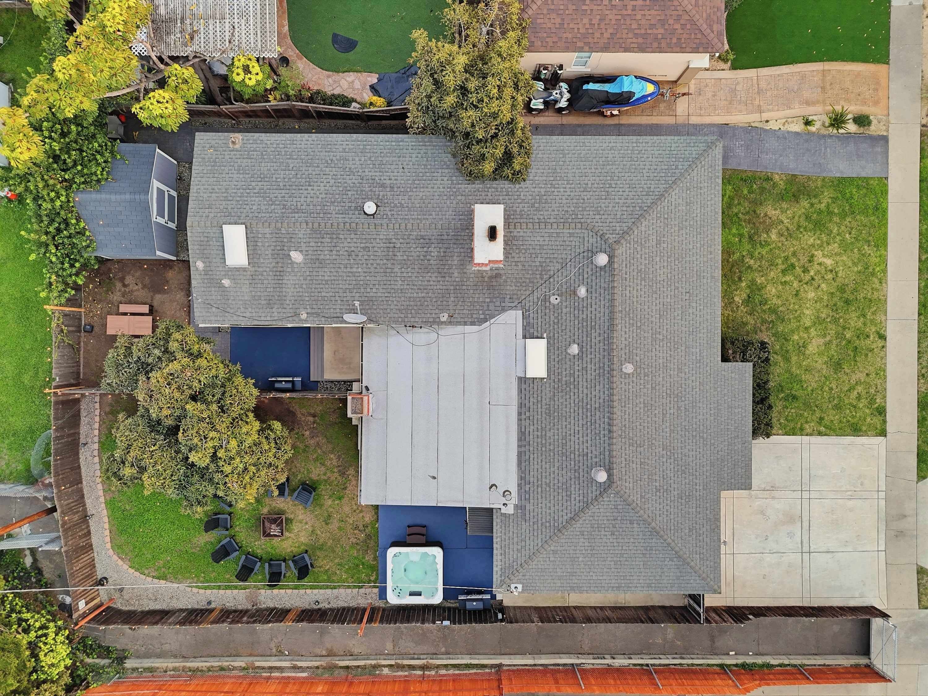 An aerial view of a residential property with a sloped roof, a hot tub, outdoor seating, and a fenced yard.