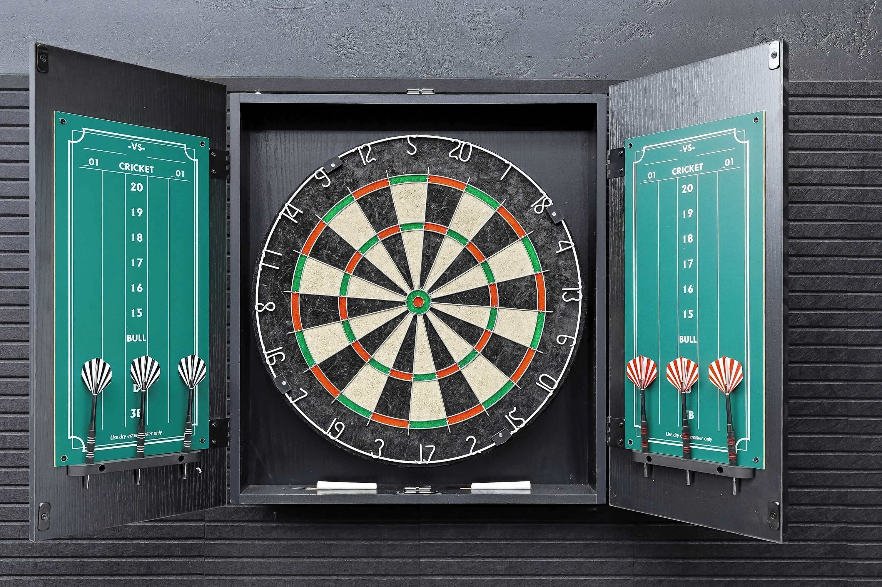 Eine Dartscheibe mit Anzeigetafel und drei Dartspielen an der Wand.