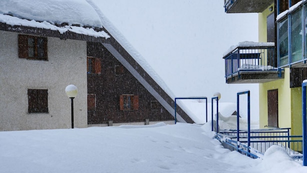 Un espacio exterior nevado con un edificio de varias ventanas y una escalera que conduce a un balcón.