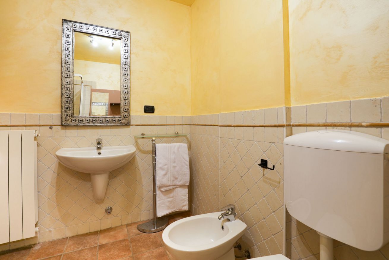 Een badkamer met een wastafel, bidet, toilet en een spiegel met decoratieve lijst.