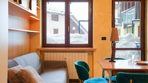 Una habitación acogedora con sofá, una mesa de comedor con sillas y una ventana con vista a un edificio nevado.