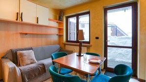Un salón acogedor con sofá, sillas color aguamarina, una mesa de madera y una ventana con vistas a un paisaje nevado.