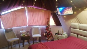 Une pièce confortable avec un lit, deux fauteuils, une petite table, un sapin de Noël et un téléviseur fixé au mur.