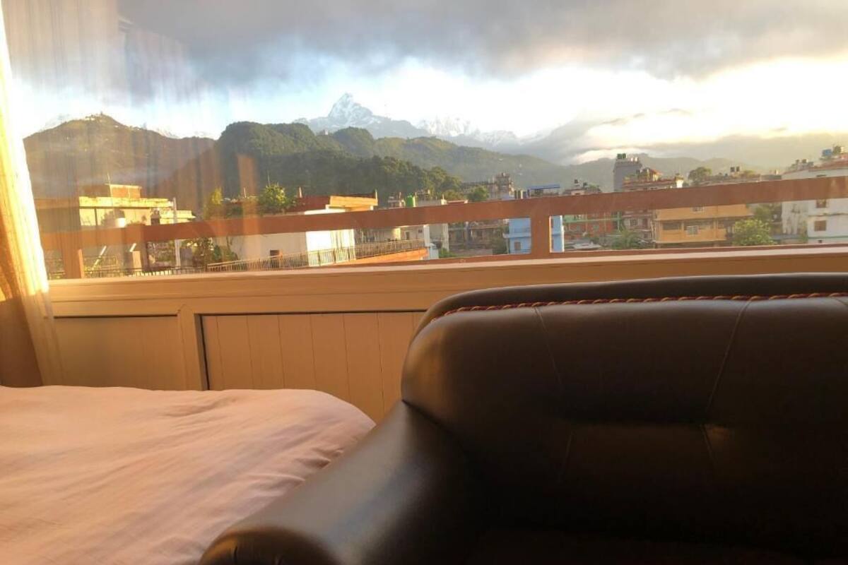 A hotel room with a bed and a leather chair, a view of a cityscape and mountains through a window.