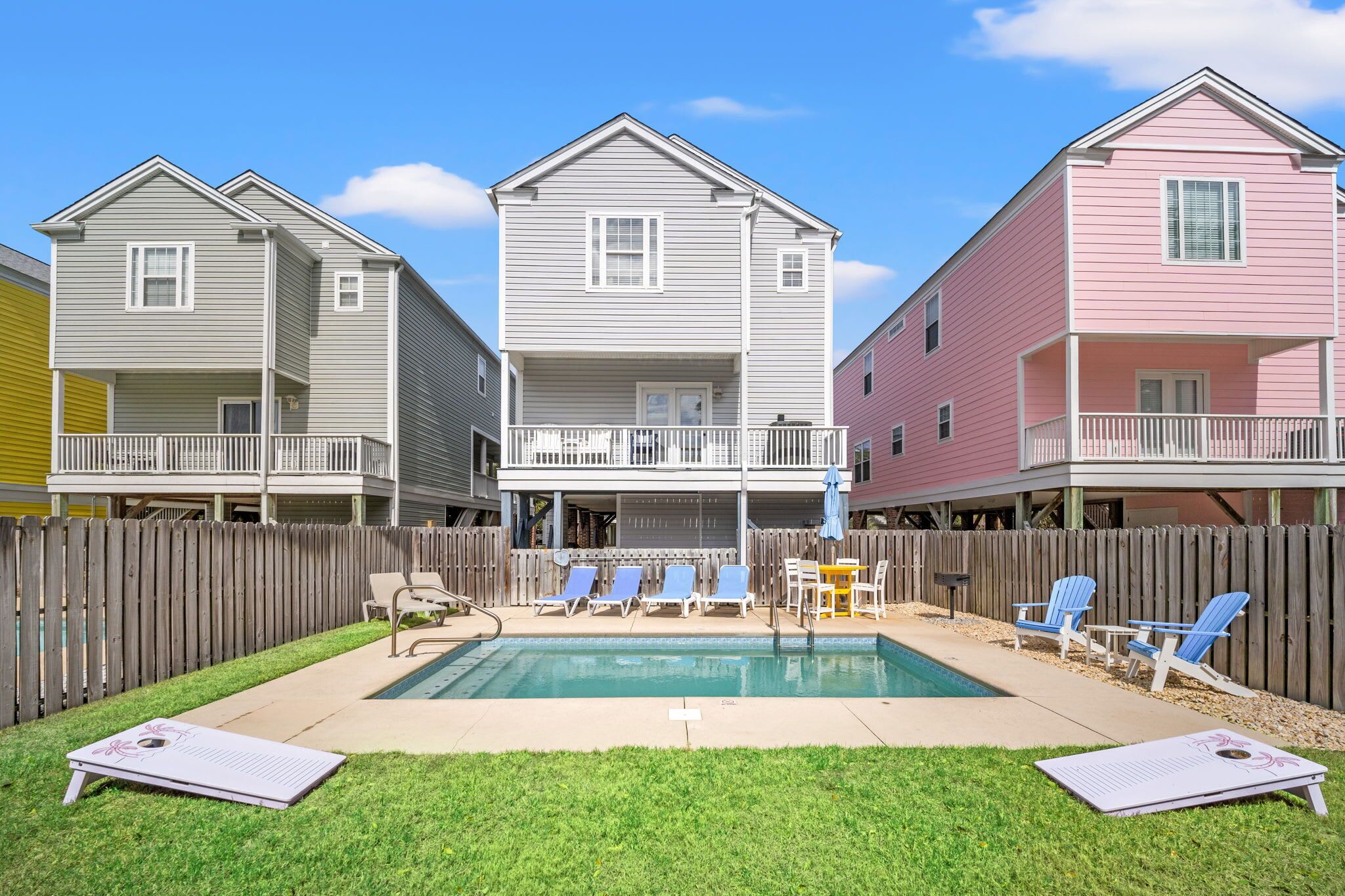 Un barrio residencial con tres casas, una piscina y mobiliario exterior.