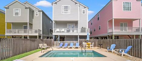 Un barrio residencial con tres casas, una piscina y mobiliario exterior.
