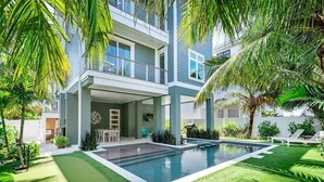 Una casa moderna de dos pisos con piscina, rodeada de exuberante vegetación y palmeras.