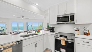 A modern kitchen with white cabinets, a stainless steel sink, a microwave, and an oven. - Infinite Views! Heated Pool! Directly on Tampa Bay (Holmes Beach)