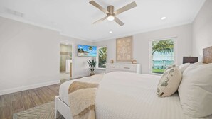 A spacious bedroom with a large bed, a ceiling fan, a TV, and a view of the outdoors. - Infinite Views! Heated Pool! Directly on Tampa Bay (Holmes Beach)