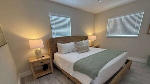 Quarto com uma cama grande, duas mesas de cabeceira e duas janelas com persianas.