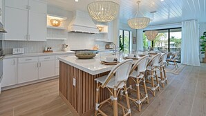Una cucina moderna con mobili bianchi, un'isola centrale con sgabelli da bar e grandi lampade a sospensione.