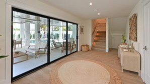 Un'ampia zona giorno con una grande porta a vetri scorrevoli che si apre su un patio esterno con piscina, una scala e un piccolo tavolino con oggetti decorativi.