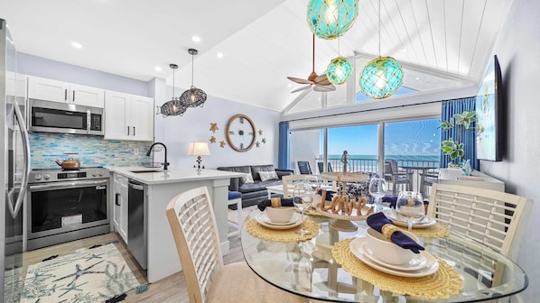 A modern kitchen with stainless steel appliances, a dining area with a glass table, and a view of the ocean.