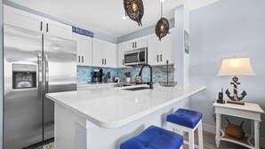 A modern kitchen with a large island, stainless steel appliances, and a blue accent wall. - New! Beachfront Paradise! ~Heated Pool! Top Floor (Holmes Beach)