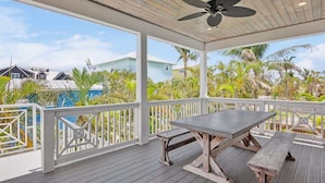 A covered outdoor area with a wooden table and benches, surrounded by white railings and palm trees. - Atlantis Beach House~Water Slide, Heated Pool/Spa! (Bradenton Beach)
