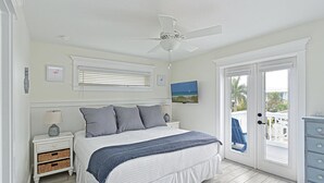 A bedroom with a bed, nightstands, a ceiling fan, a window with blinds, and a door leading to a balcony. - Atlantis Beach House~Water Slide, Heated Pool/Spa! (Bradenton Beach)