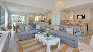 A spacious living room with a grey sofa set, a white coffee table, and a large woven pendant light. - Atlantis Beach House~Water Slide, Heated Pool/Spa! (Bradenton Beach)