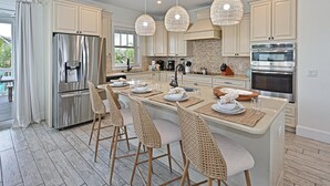 A modern kitchen with a central island, bar stools, stainless steel appliances, and pendant lighting. - Atlantis Beach House~Water Slide, Heated Pool/Spa! (Bradenton Beach)