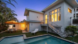 Ett modernt hus med en swimmingpool, en täckt uteplats och en trappa som leder upp till en balkong.
