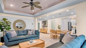 A spacious living room with a blue sofa, a coffee table, and a ceiling fan. - Birdsong-Steps to Bean Point Beach Heated Pool! (Anna Maria)