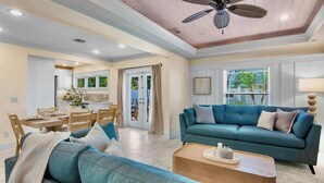 A spacious living room with a teal sofa, a wooden coffee table, and a ceiling fan. - Birdsong-Steps to Bean Point Beach Heated Pool! (Anna Maria)