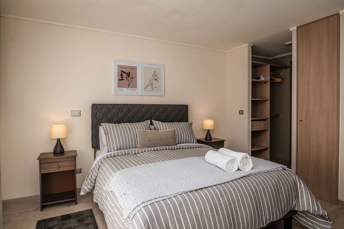 Een netjes ingerichte slaapkamer met een bed, twee nachtkastjes, een kledingkast en twee kunstwerken in lijsten aan de muur.