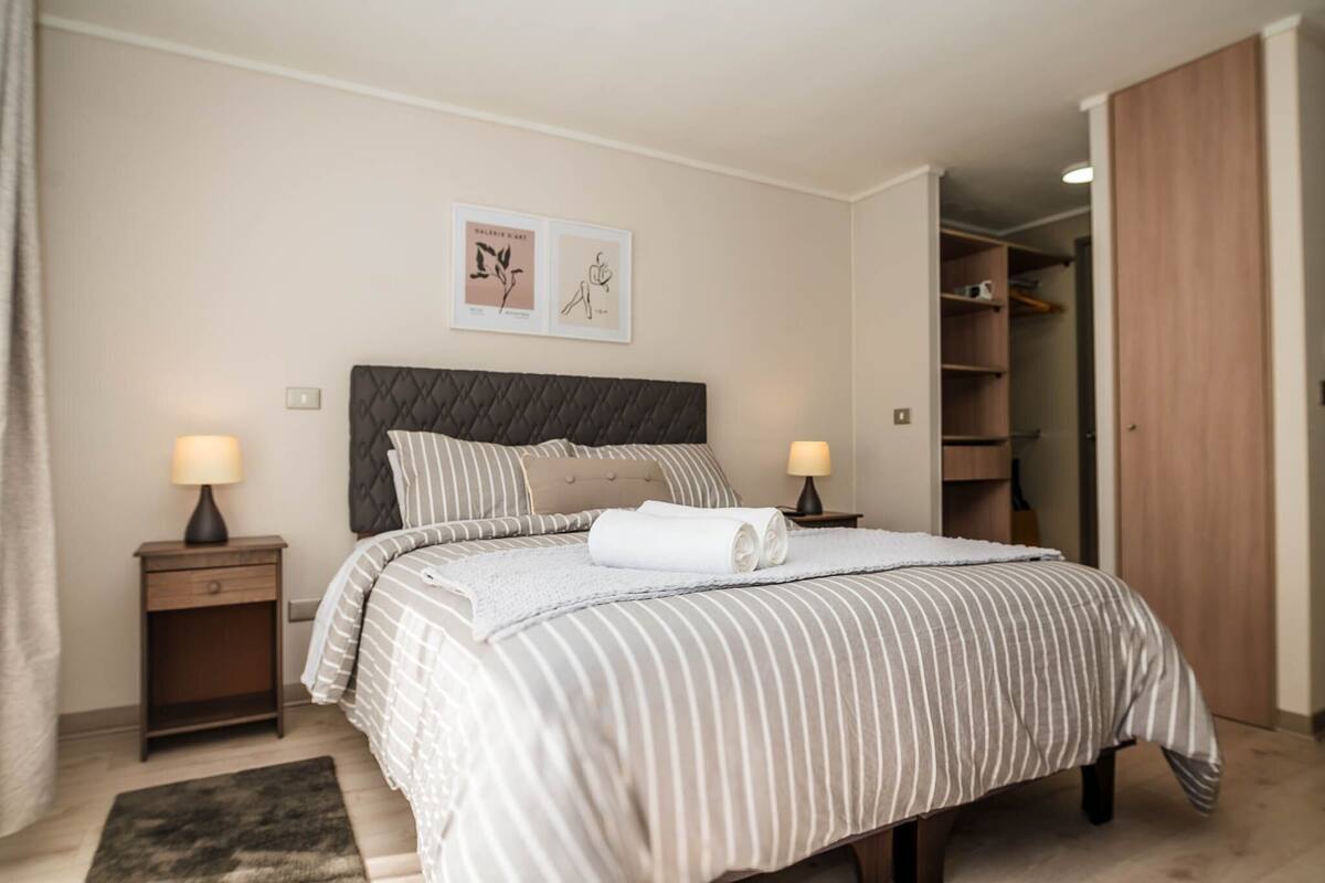 Een slaapkamer met een bed, twee nachtkastjes, een kledingkast en een deur die naar een andere kamer leidt.