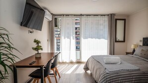Hotelkamer met een bed, een bureau met stoel, een potplant, een aan de muur bevestigde televisie en een balkon met gordijnen.
