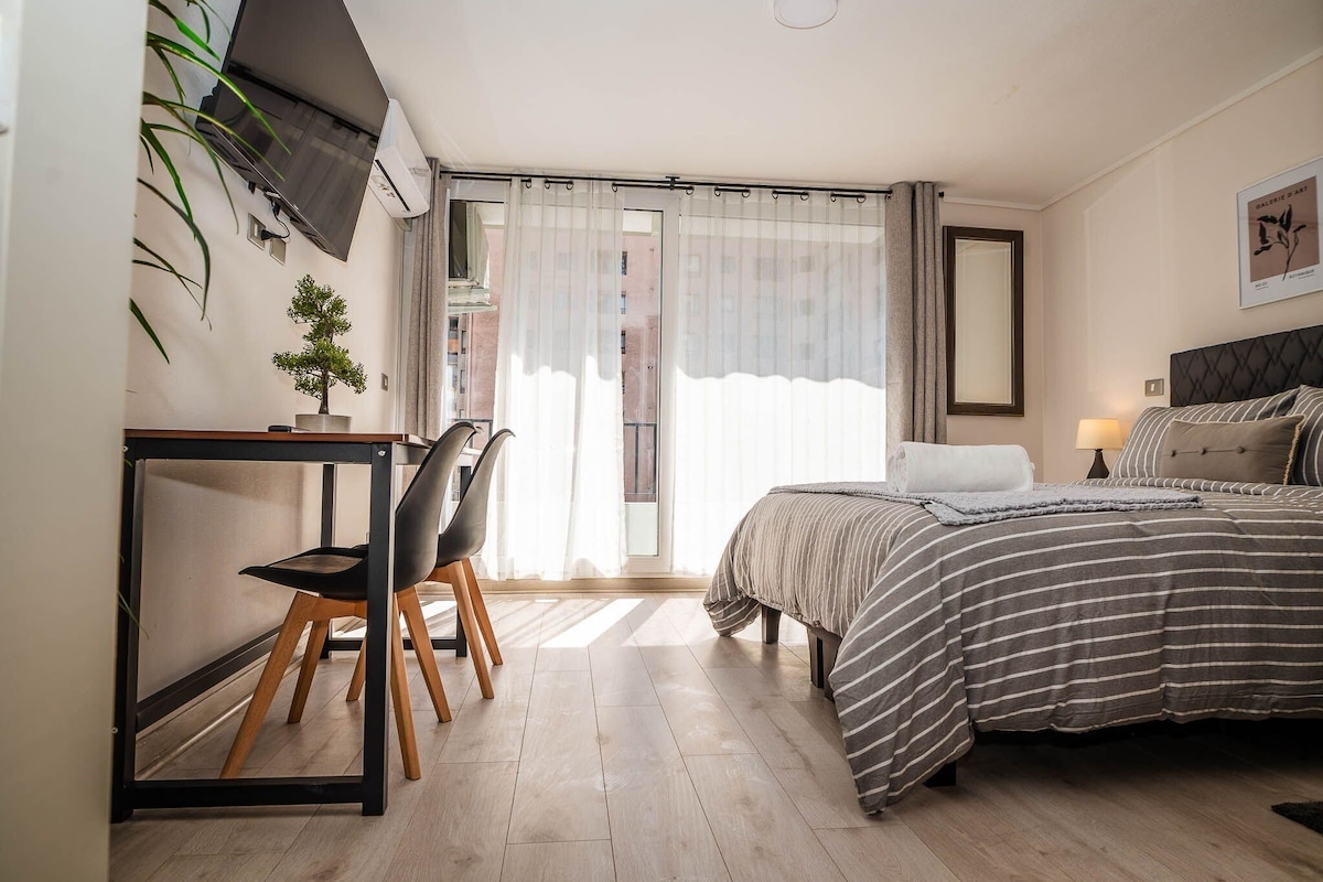 A modern bedroom with a bed, a desk, a chair, and a potted plant.