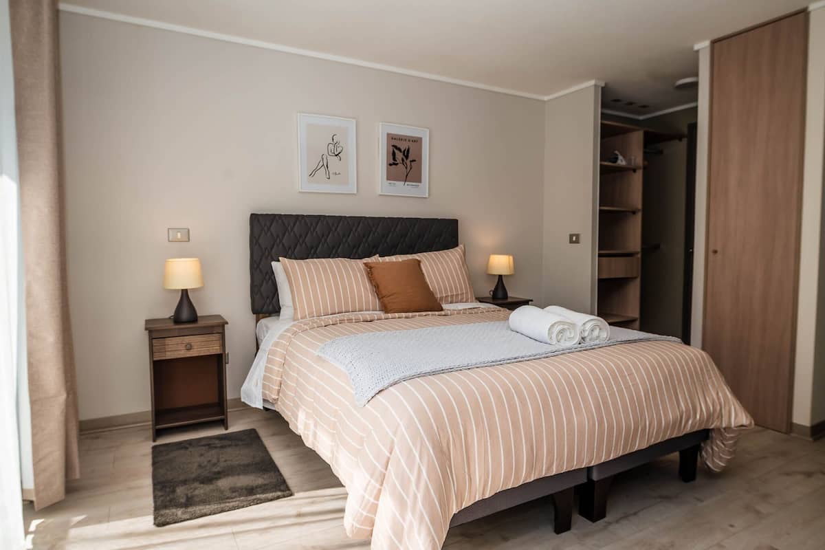 Een opgemaakt bed met gestreept beddengoed, twee bedlampen en een donker hoofdbord.