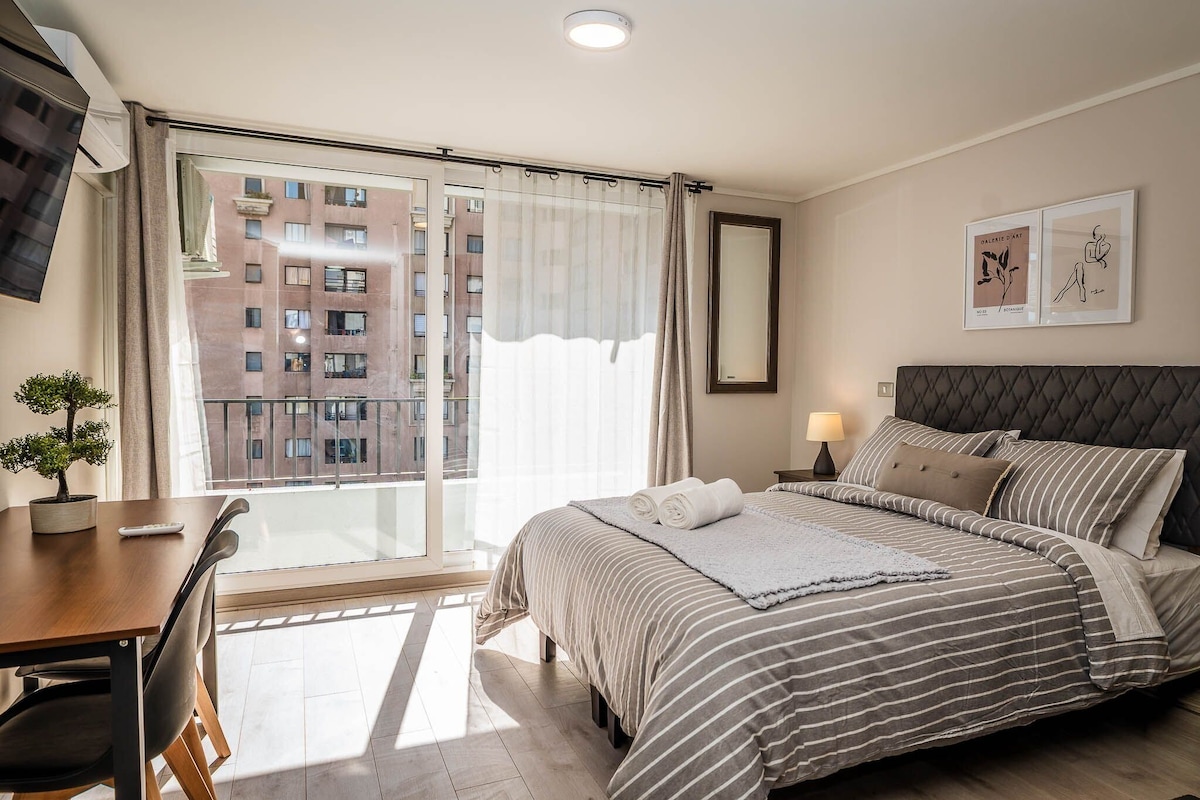 A hotel room with a large bed, a desk, and a view of a building through a window.