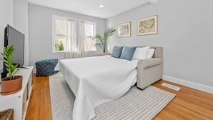 A modern bedroom with a large bed, a sofa, a TV, and a potted plant. - Boston Condo with Free Parking (Boston)