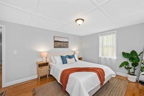 A bedroom with a bed, bedside tables, a nightstand, a window, and a plant. - Boston Condo with Free Parking (Boston)