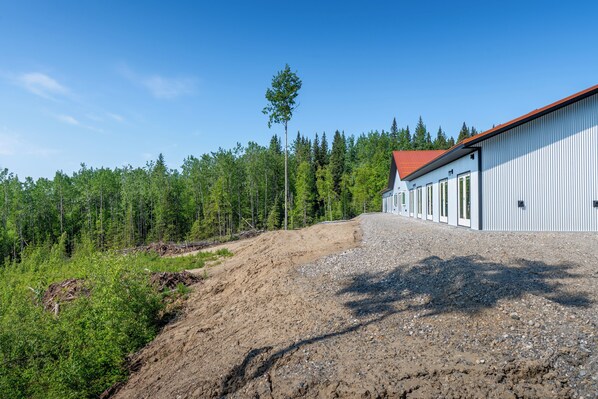 A building with a red roof, surrounded by a forest and a gravel path. - The Orion (Fairbanks)