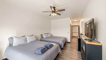 Habitación de hotel con dos camas, ventilador de techo, televisor de pantalla plana y piso de madera.