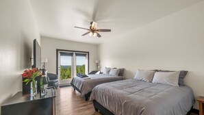 Une chambre avec deux lits, un bureau agrémenté d’un vase de fleurs, un ventilateur de plafond et une vue sur l’extérieur.