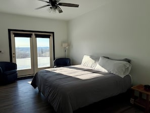 Een slaapkamer met een bed, een plafondventilator, een stoel, een nachtkastje en uitzicht door een schuifdeur.