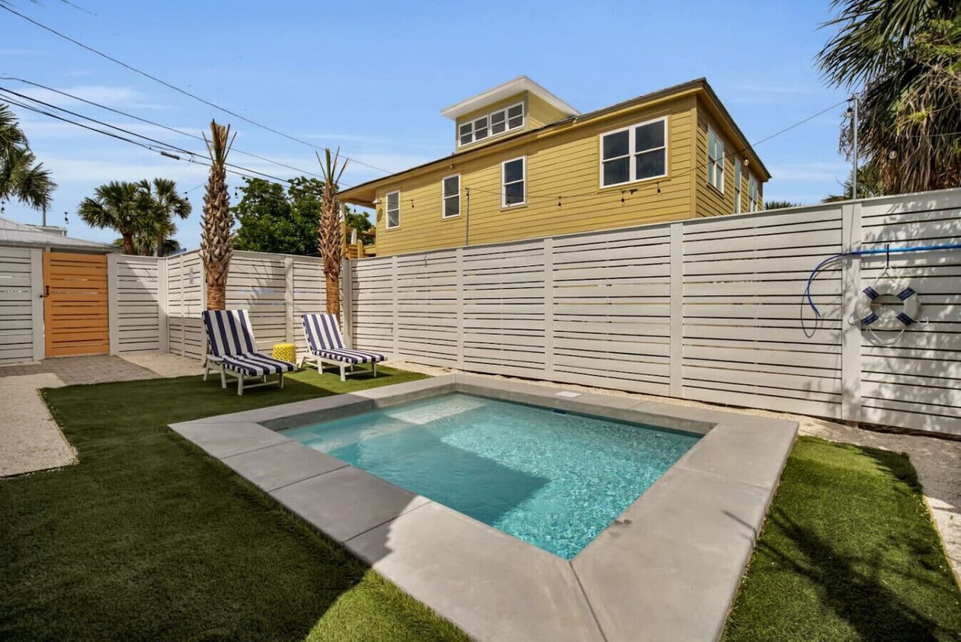 A rectangular swimming pool with two lounge chairs and a wooden gate in a backyard.